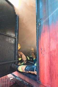 Firefighters sitting in metal structure filled with heavy smoke during a training exercise.